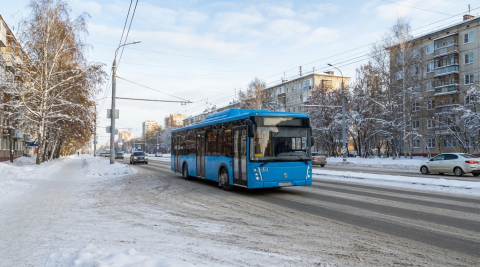 Синий небольшой автобус едет по заснеженной улице в морозный солнечный день 