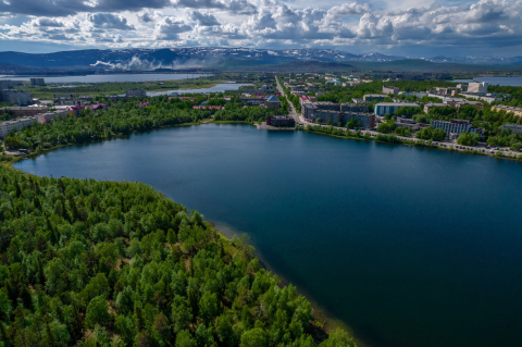 Комсомольское озеро в Мончегорске с высоты среди леса и городских кварталов 