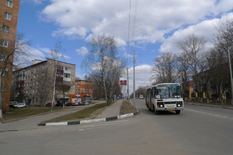 Маленький автобус едет по пустой улице небольшого города мимо пятиэтажек весной 