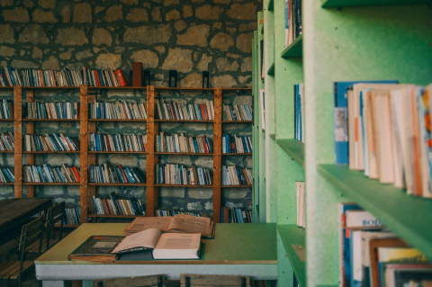 Стол с раскрытыми книгами среди стеллажей в небольшой библиотеке 