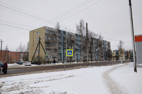 Панельный дом в посёлке зимой, заснеженный тротуар и пешеходный переход у дороги 