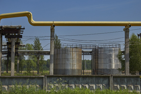 Жёлтая труба газопровода на опорах над бетонным забором, за ним металлические резервуары 
