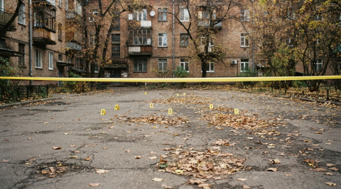 Жёлтые номерки улик на асфальте во дворе за лентой ограждения 