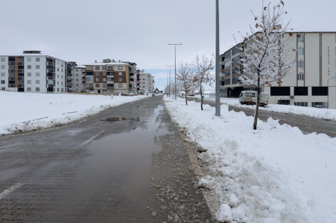 Слякоть на городской улице: мокрый асфальт, лужи и сугробы у тротуара среди новостроек 