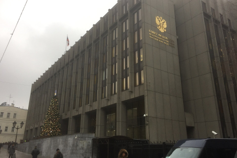 Здание верхней палаты парламента с гербом на фасаде и новогодней елью у входа в пасмурный день 