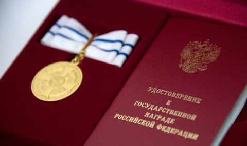 Золотая медаль на бело-голубой ленте в футляре рядом с красным удостоверением к госнаграде 