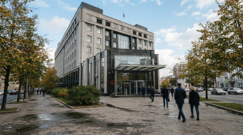 Современное административное здание с большими окнами, у входа идут пешеходы осенним днём 