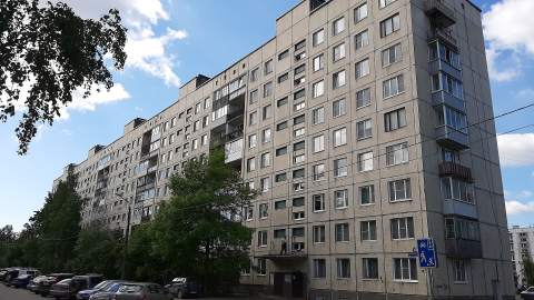 Длинная серая панельная девятиэтажка с подъездами и машинами во дворе летом 