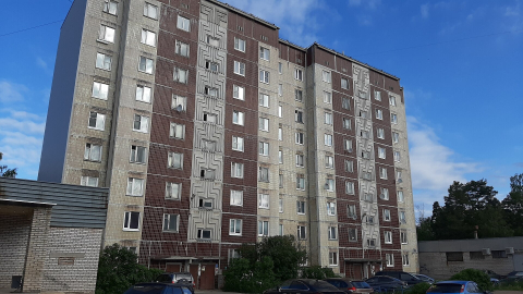 Панельная девятиэтажка с красно-коричневыми полосами на фоне ярко-синего неба 