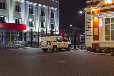 Полицейский внедорожник ночью у ограды освещённого здания на пустой площади 