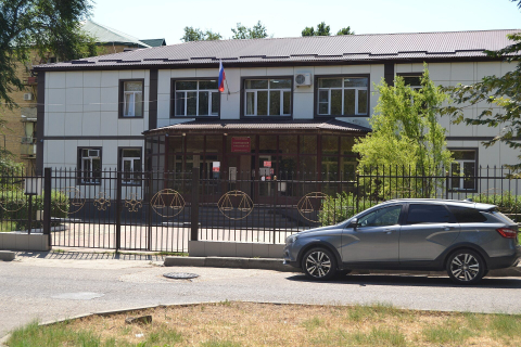 Одноэтажное здание городского суда за кованой оградой, флаг над входом и машина у ворот 