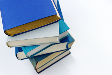 Книги в синих и голубых твёрдых переплётах сложены стопкой на белом столе 