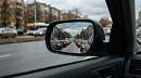 В боковом зеркале машины отражается длинная пробка из стоящих автомобилей 