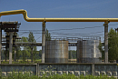 Жёлтая труба газопровода на опорах над бетонным забором, за ним металлические резервуары 