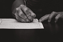 Чёрно-белый кадр, морщинистые руки пожилого человека заполняют бланк 